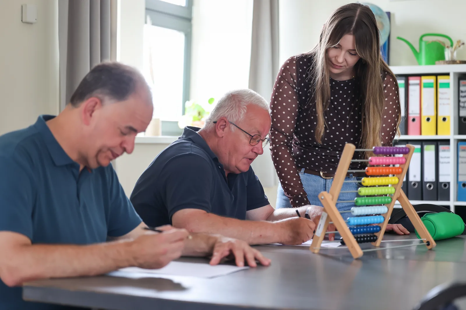 Zwei Teilnehmer arbeiten konzentriert am Tisch, eine Betreuerin unterstützt, in der Tagesförderstätte Klennow