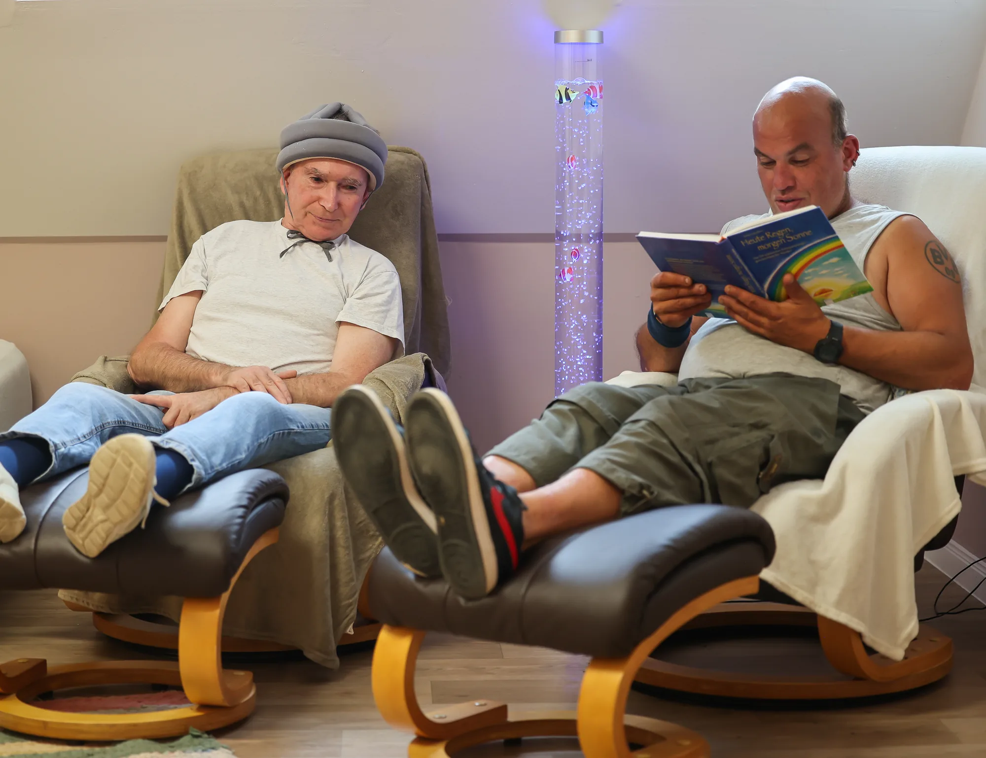 Zwei Bewohner entspannen in Sesseln im Snoezelen-Raum, einer liest ein Buch