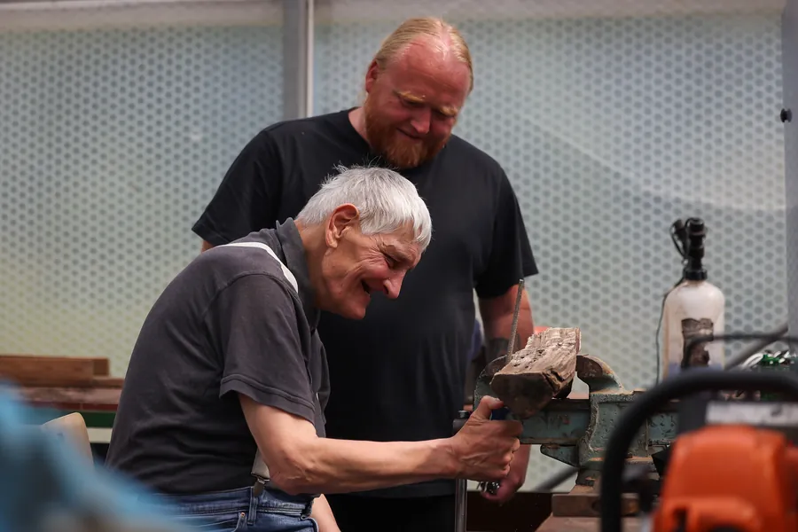 Älterer Bewohner und Mitarbeiter lachen in der Holzwerkstatt